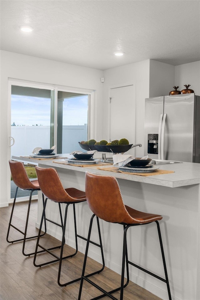 kitchen with stainless steel refrigerator with ice dispenser, light wood-type flooring, a textured ceiling, and a kitchen bar