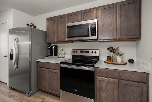 kitchen featuring dark brown cabinetry, stainless steel appliances, light hardwood / wood-style floors, and a textured ceiling