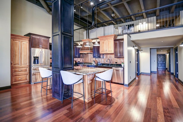 kitchen with appliances with stainless steel finishes, a towering ceiling, light stone countertops, and dark hardwood / wood-style flooring