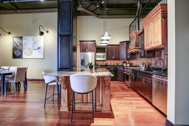 kitchen with light hardwood / wood-style flooring, stainless steel appliances, hanging light fixtures, and light stone countertops