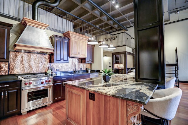 kitchen featuring premium stove, dark wood-type flooring, a breakfast bar area, tasteful backsplash, and dark stone countertops