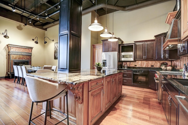 kitchen featuring appliances with stainless steel finishes, a kitchen island, light hardwood / wood-style floors, dark stone counters, and a high ceiling