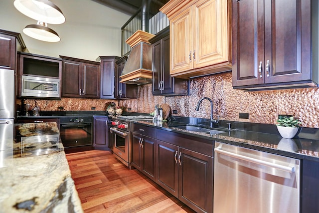 kitchen featuring appliances with stainless steel finishes, sink, backsplash, light wood-type flooring, and premium range hood