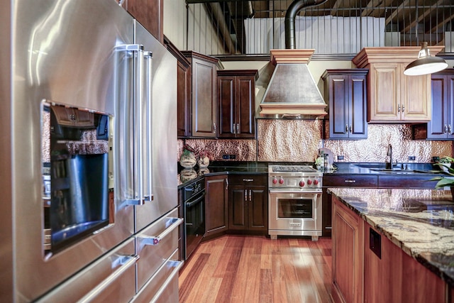 kitchen with high end appliances, pendant lighting, light hardwood / wood-style flooring, sink, and dark stone countertops