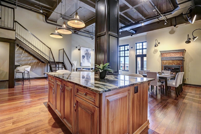 kitchen with hanging light fixtures, dark stone counters, light wood-type flooring, and a high ceiling