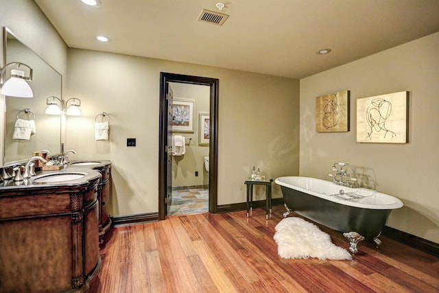 bathroom with a bath to relax in, wood-type flooring, and dual vanity