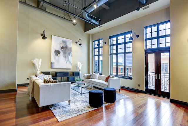 living room featuring wood-type flooring, french doors, and a high ceiling