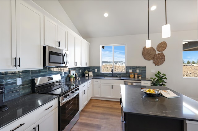 kitchen with vaulted ceiling, appliances with stainless steel finishes, sink, white cabinets, and hanging light fixtures