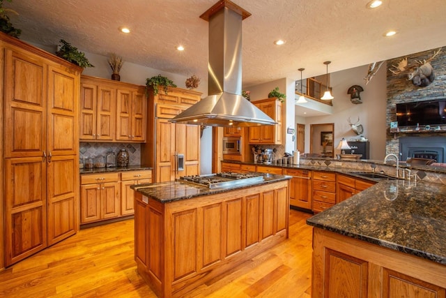 kitchen with pendant lighting, island range hood, appliances with stainless steel finishes, sink, and light hardwood / wood-style floors