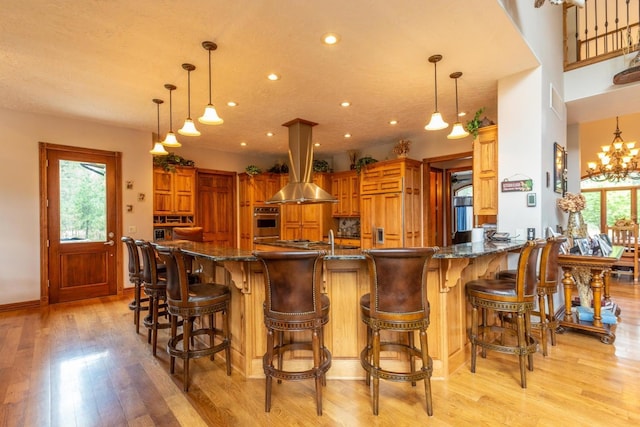 kitchen with island exhaust hood, a healthy amount of sunlight, stainless steel oven, and pendant lighting