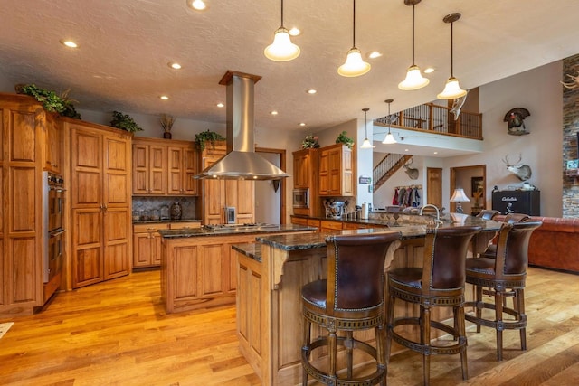 kitchen with kitchen peninsula, light hardwood / wood-style flooring, a breakfast bar area, pendant lighting, and island exhaust hood