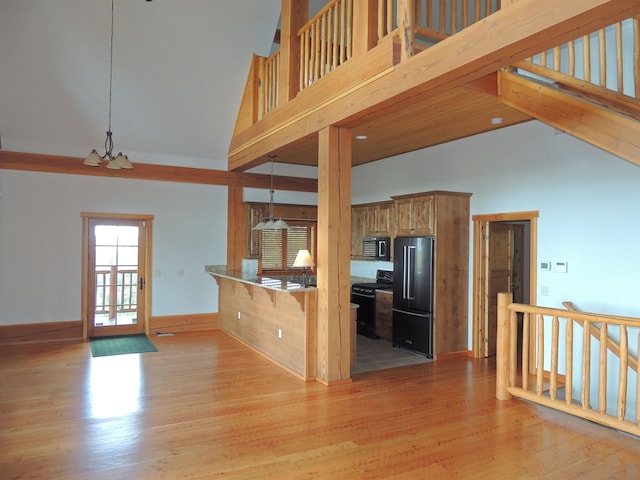 kitchen featuring high vaulted ceiling, hanging light fixtures, high end black refrigerator, and hardwood / wood-style flooring