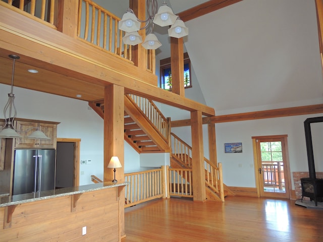 interior space with high vaulted ceiling, wood-type flooring, a chandelier, and a wood stove