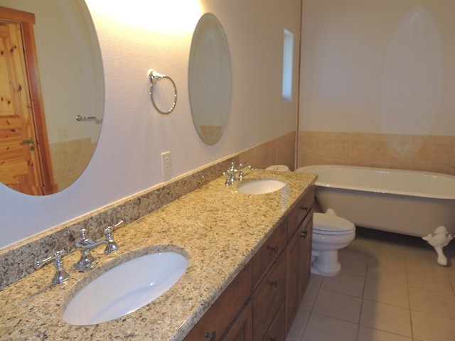 bathroom featuring tile flooring, double sink, vanity with extensive cabinet space, a bathtub, and toilet