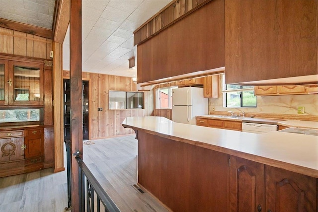 kitchen with kitchen peninsula, white appliances, sink, light hardwood / wood-style floors, and wood walls