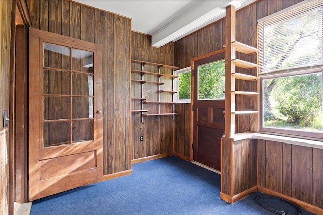 entryway featuring dark colored carpet, beam ceiling, and wooden walls