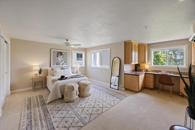 bedroom featuring ceiling fan, built in desk, light carpet, and a textured ceiling