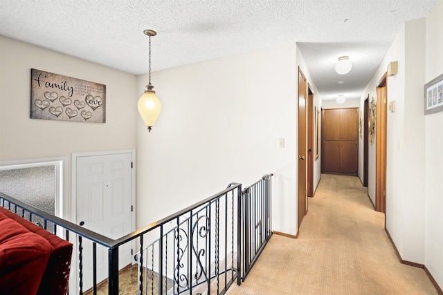 hall with an upstairs landing, baseboards, a textured ceiling, and light colored carpet