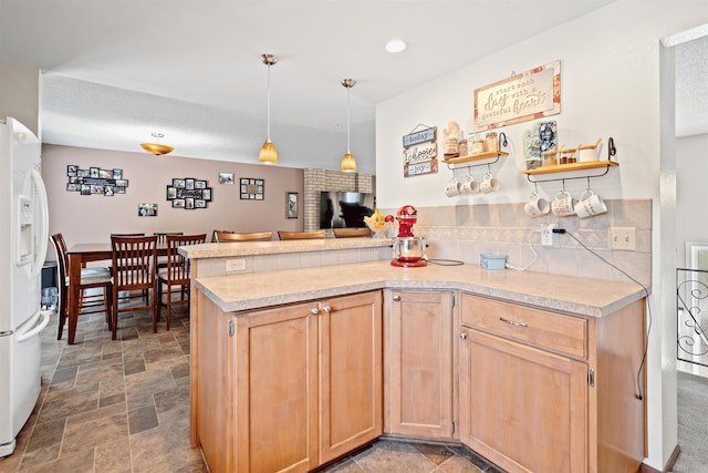 kitchen featuring a peninsula, stone finish flooring, light countertops, light brown cabinetry, and white fridge with ice dispenser