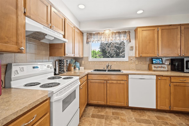 kitchen featuring white appliances, tasteful backsplash, light countertops, under cabinet range hood, and a sink