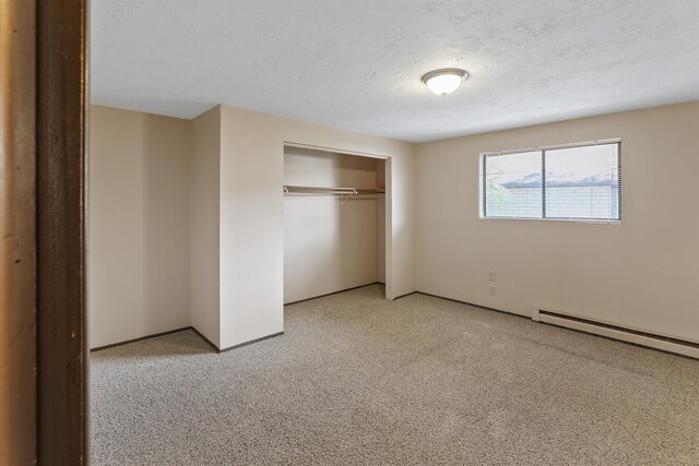 unfurnished bedroom featuring a baseboard radiator, a textured ceiling, a closet, and light colored carpet