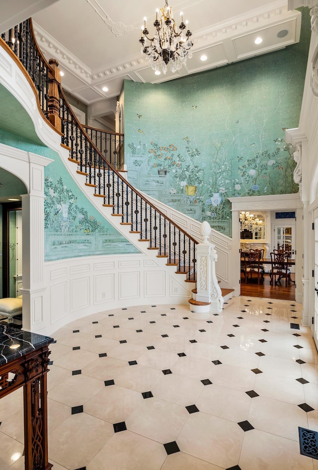 staircase with a towering ceiling, a notable chandelier, light tile patterned floors, and ornamental molding