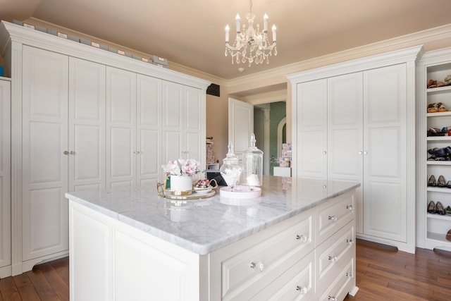 kitchen with dark wood-type flooring, light stone countertops, a kitchen island, and ornamental molding