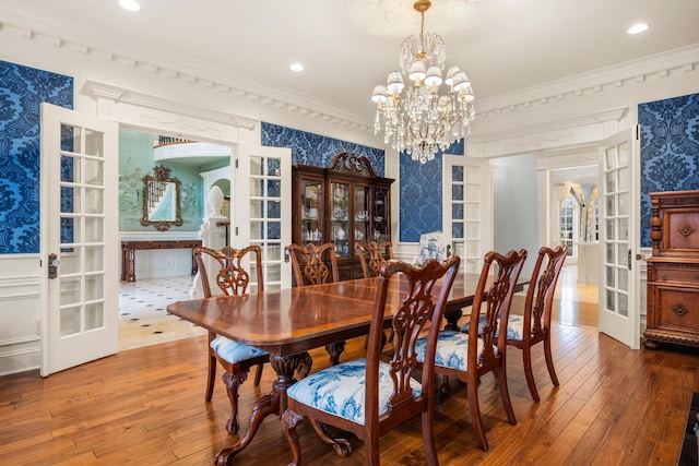 dining area with hardwood / wood-style flooring, ornamental molding, an inviting chandelier, and french doors