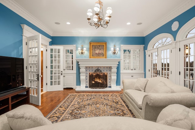 living room featuring a notable chandelier, french doors, a fireplace, hardwood / wood-style flooring, and ornamental molding