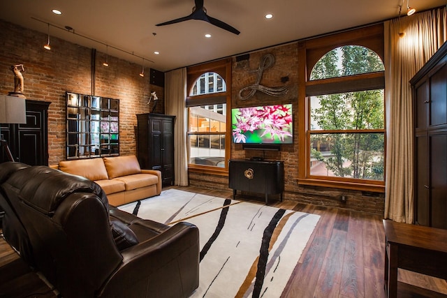 living room with brick wall, hardwood / wood-style flooring, a towering ceiling, and ceiling fan