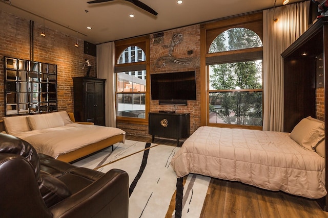 bedroom featuring brick wall, a wood stove, wood-type flooring, and a high ceiling