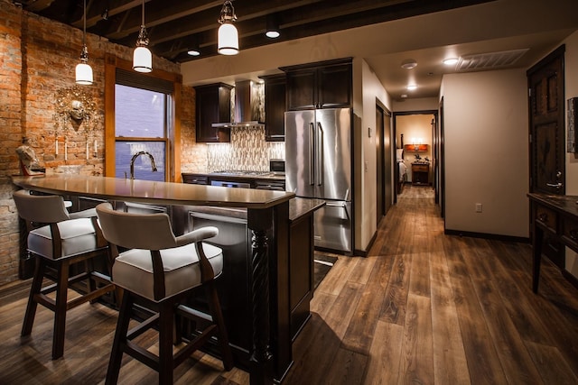 kitchen featuring wall chimney range hood, dark hardwood / wood-style flooring, stainless steel appliances, hanging light fixtures, and a kitchen bar