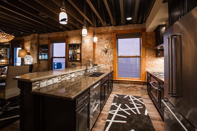 kitchen with decorative light fixtures, sink, dark stone countertops, appliances with stainless steel finishes, and light hardwood / wood-style flooring