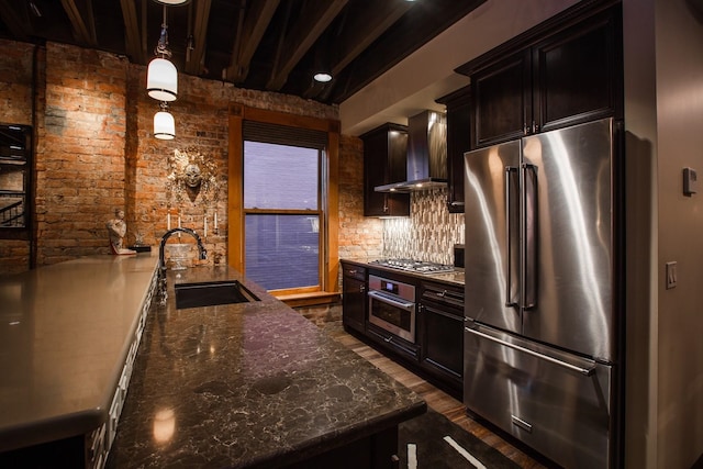 kitchen with decorative light fixtures, stainless steel appliances, wall chimney exhaust hood, brick wall, and sink