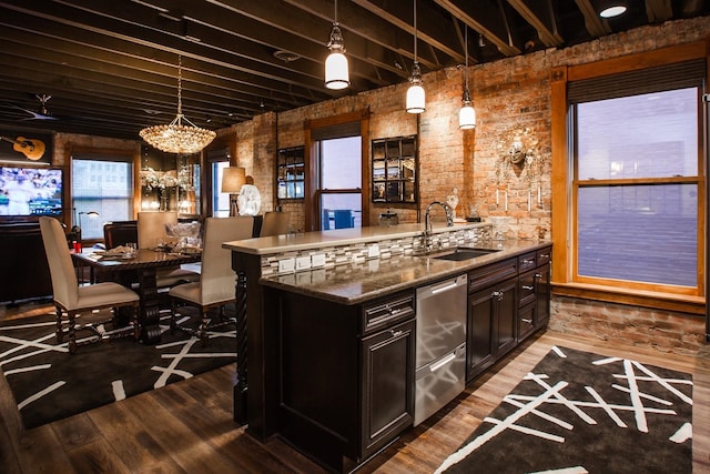 kitchen with a chandelier, hanging light fixtures, hardwood / wood-style floors, brick wall, and sink