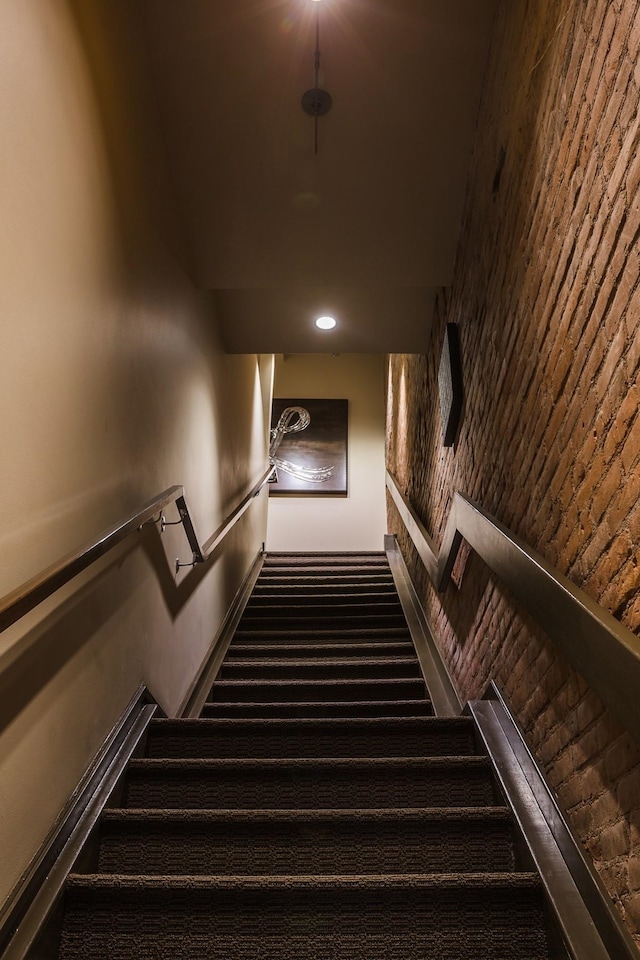 stairs with carpet flooring and brick wall