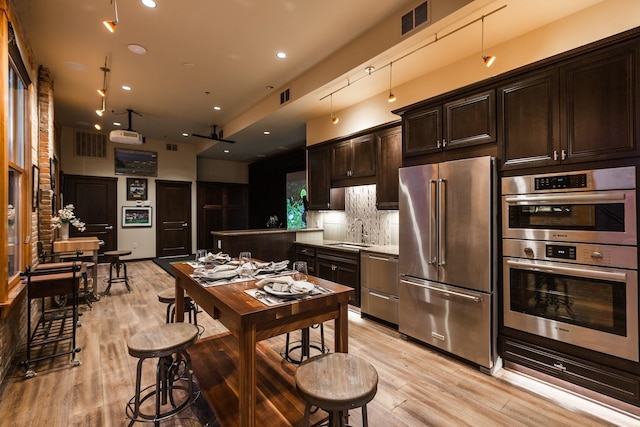 kitchen featuring dark brown cabinets, tasteful backsplash, sink, light hardwood / wood-style floors, and appliances with stainless steel finishes