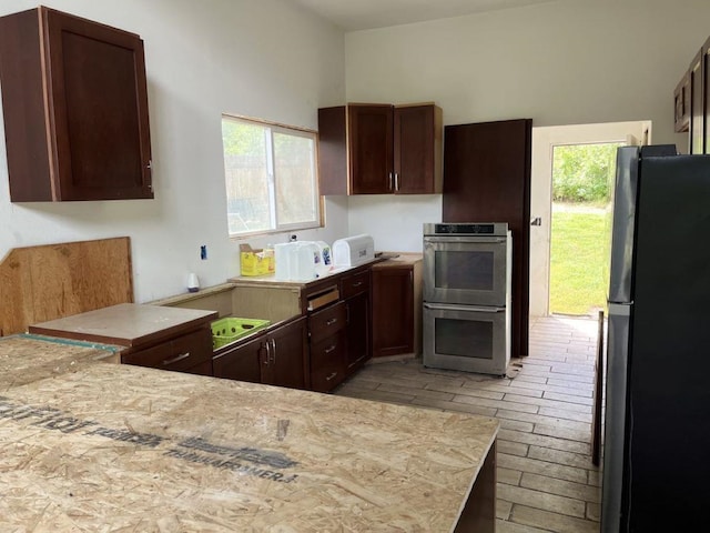 kitchen with dark brown cabinetry, stainless steel double oven, kitchen peninsula, and black refrigerator