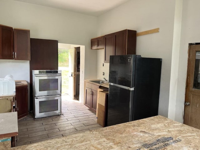 kitchen featuring range, sink, stainless steel double oven, and black fridge