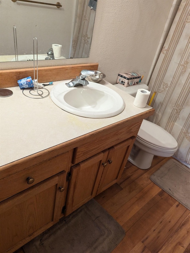 bathroom featuring toilet, a textured wall, wood finished floors, and vanity