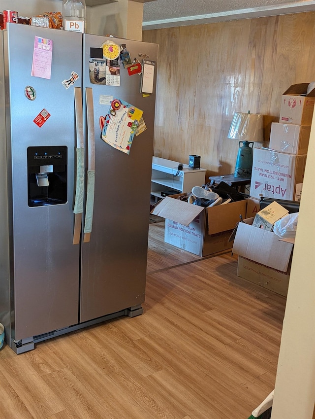 kitchen with stainless steel fridge, wooden walls, and wood finished floors