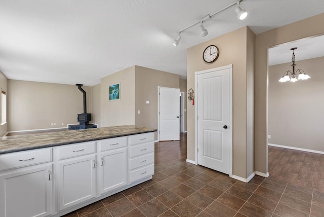 kitchen featuring white cabinetry, a wood stove, hanging light fixtures, a notable chandelier, and a textured ceiling