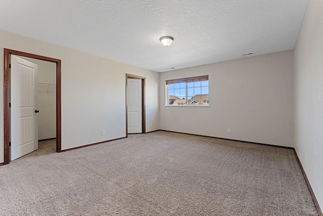 unfurnished bedroom featuring light colored carpet, a spacious closet, a closet, and a textured ceiling