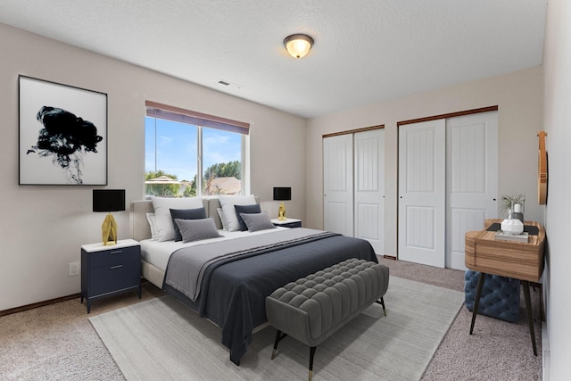 bedroom with light carpet, two closets, and a textured ceiling