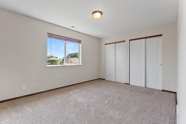 unfurnished bedroom with multiple closets, carpet flooring, and a textured ceiling