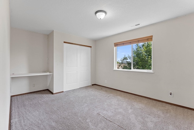 unfurnished bedroom featuring light colored carpet, built in desk, and a closet