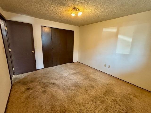 unfurnished bedroom with a textured ceiling, a closet, and light colored carpet