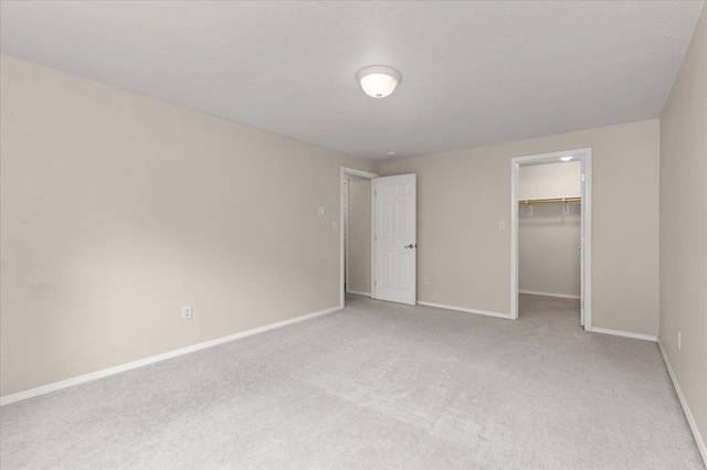 unfurnished bedroom featuring light carpet, a walk in closet, a closet, and a textured ceiling