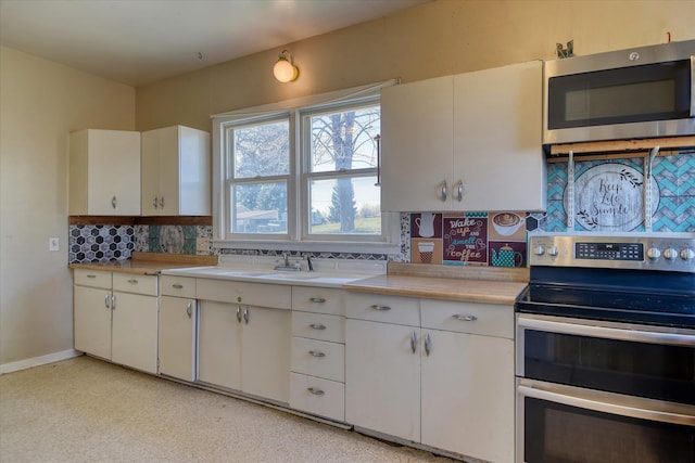 kitchen featuring stainless steel appliances, light countertops, backsplash, white cabinetry, and a sink