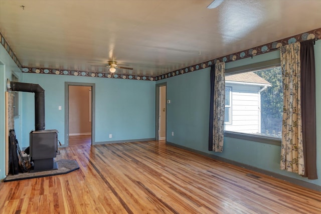 unfurnished living room featuring baseboards, wood finished floors, a wood stove, and a ceiling fan